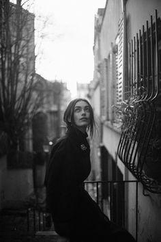 black and white photograph of a woman leaning against a wall in an alleyway looking up at the sky