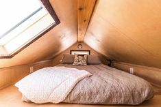 a bed with a white comforter and pillows in a small room under a slanted roof