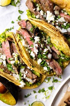 three steak tacos with cilantro, lime and feta cheese on top