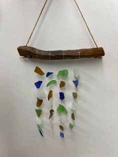 a piece of driftwood hanging from a wall with sea glass pieces on it and a stick attached to the wall