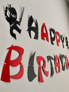 happy birthday banner with black and red paper cutouts hanging on the side of a white wall