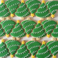 decorated christmas tree cookies arranged in rows on a white tablecloth with yellow stars and green frosting