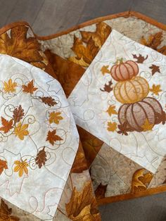 three quilted coasters with autumn leaves and pumpkins on them, sitting on a table