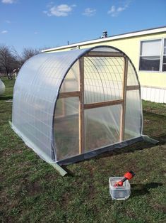 a small greenhouse in the middle of a yard next to a building with windows on it