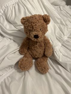 a brown teddy bear sitting on top of a white bed cover covered in sheets and pillows