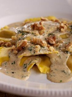 a white plate topped with ravioli covered in gravy and chopped walnuts