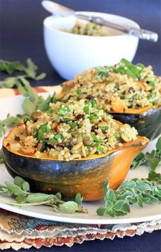 two squash filled with rice and vegetables on a plate next to a bowl of greens