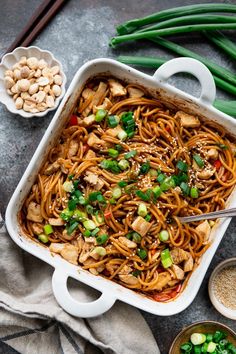 a pan filled with noodles and vegetables next to some chopsticks on the side