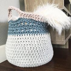 a crocheted basket with a white, blue and pink handle sits on a wooden floor