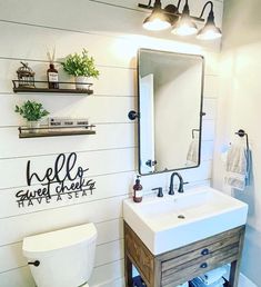 a white toilet sitting under a bathroom mirror next to a wooden sink vanity and wall mounted shelves