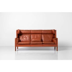 an orange leather couch with wooden legs and arm rests on a white floor in front of a wall