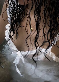 a woman is sitting in the water with her hair flowing over her face and wearing a white dress