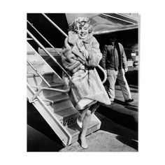 an old photo of a woman in fur coat walking down the stairs at an airport