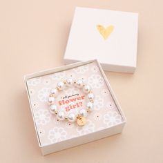 a white box with a gold heart charm on it and a bracelet that says flower girl