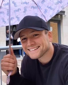 a man holding an umbrella in front of him and smiling at the camera while sitting down