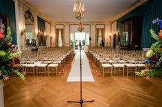 an empty room with rows of chairs and a microphone in the foreground, surrounded by floral arrangements