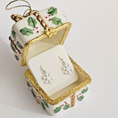 a pair of christmas themed earrings in a gift box with holly decorations on the sides