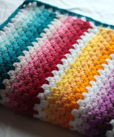 a multicolored crocheted blanket laying on top of a bed