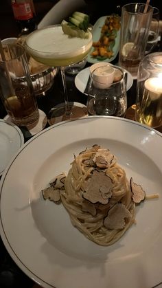 a white plate topped with pasta covered in sauce and toppings next to wine glasses