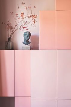 a vase sitting on top of a pink cabinet next to a vase filled with flowers