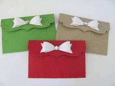 three different colored envelopes with white bows on them and one has a bow tie