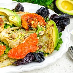 a white plate topped with an orange and avocado salad next to other vegetables