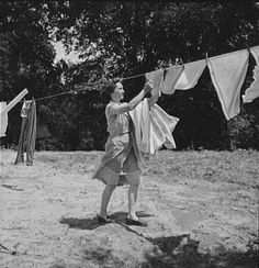 an old black and white photo of a woman hanging clothes on a line with her hands