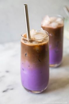 two glasses filled with purple liquid and topped with ice cubes on a marble surface