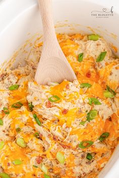 a wooden spoon in a casserole dish filled with chicken and cheese, garnished with green onions