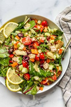 a white bowl filled with salad and topped with lemon wedges