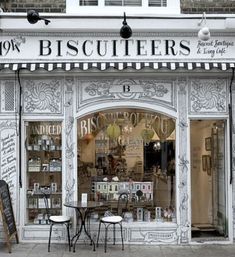 the front of a store with tables and chairs on the sidewalk in front of it