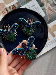 three blue and green insect brooches on a black plate