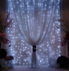 the curtains are covered with white lights in front of flowers and vases on display