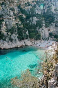 people are swimming in the clear blue water near some rocky cliffs and beachsides