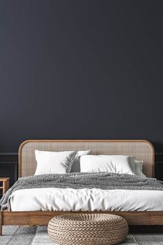 a bedroom with black walls and white bedding, wicker footstool, rattan chair and round ottoman