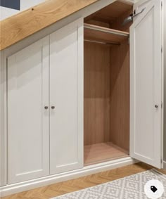 an open cabinet in the corner of a room with white walls and wood flooring