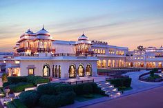 a large white building with lots of windows and lights on it's sides at dusk