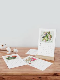 the calendar is sitting on top of a wooden table next to flowers and cotton floss