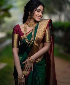 a woman in a green and gold sari with pearls on her neck, smiling