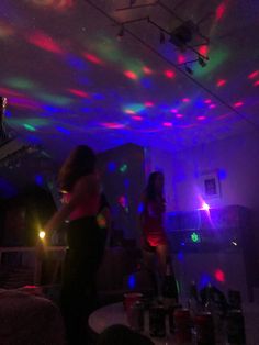 two women dancing in a room with colorful lights on the ceiling