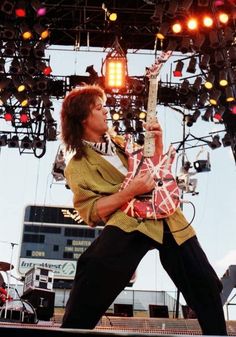 a man playing an electric guitar on stage at a music festival with lights in the background