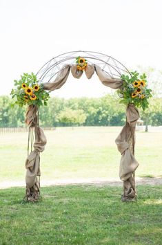 an outdoor wedding arch with sunflowers and burlocks on the top, tied to it