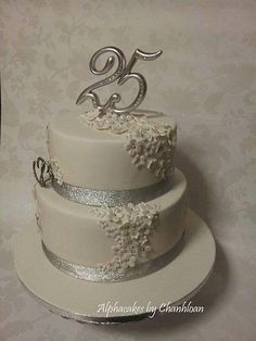 a three tiered wedding cake with silver ribbon and flowers on the top is displayed