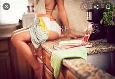 a woman sitting on top of a kitchen counter next to a coffee maker and potted plant