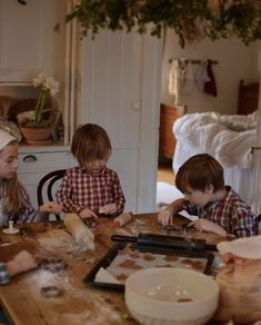 three children sitting at a table making cookies