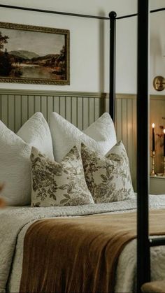 a bed with white and brown pillows in a bedroom next to a painting on the wall