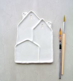 a white plate with a house on it next to a paintbrush and a pencil