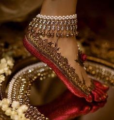 a woman's feet in gold and red shoes with jewels on the bottom, surrounded by flowers