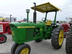 a green tractor parked in a parking lot next to other red and yellow tractors on display