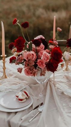 the table is set with red and pink flowers in vases, silverware, and candles